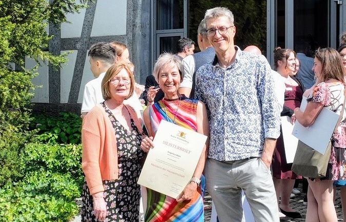 Frau mit Meisterbrief zwischen zwei Gratulanten im Freien